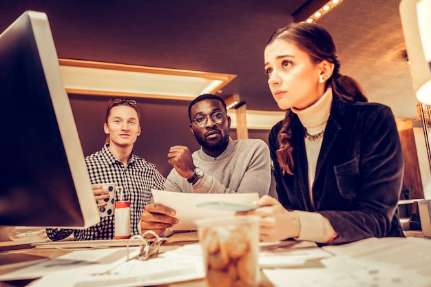 Just listen. Serious bearded man sitting between his colleagues while being in all ears