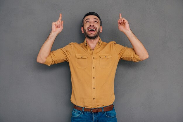 Just look at that! Happy mature man pointing up while standing against grey background