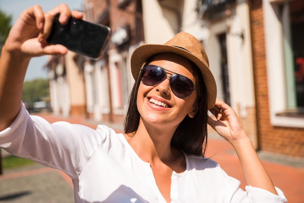 Just me and my new hat! Beautiful young funky woman adjusting her hat and making selfie while standing outdoors