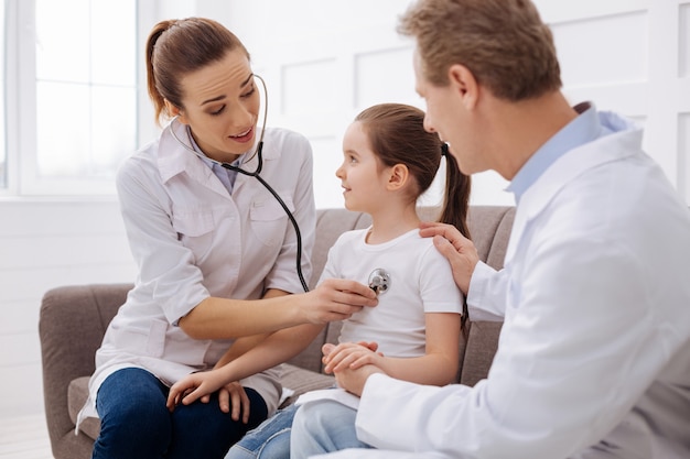 Just sit close to me. Great competent distinguished doctor running a general medical checkup and talking to little girl for her not being nervous