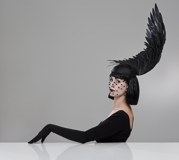 Photo just winging it shot of a young woman in a wingshaped headpiece sitting in a studio