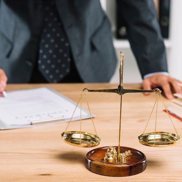 Justice scale behind the lawyer signing the document on desk