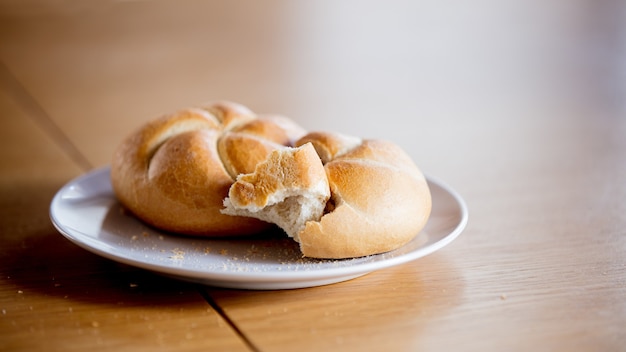 Kaiser roll on a plate on wooden table, side view