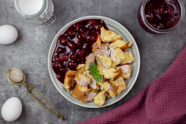 Kaiserschmarren or Kaiserschmarrn is a traditional Austrian or German sweet pancake dessert with icing sugar and berry, cherry sauce or rote grutze jam. Top view.