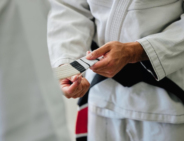 Karate master tying a belt on a student in a dojo before practice Closeup of a sensei help prepare and assisting a beginner before exercise workout and training in a sport club