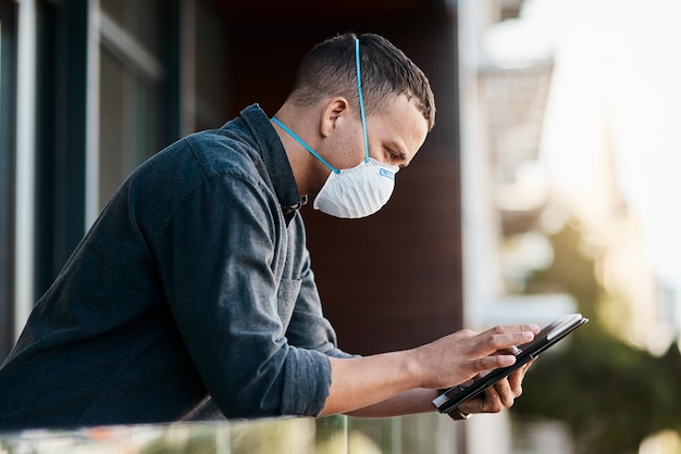 Keep on connecting no matter the circumstances Shot of a young businessman wearing a mask and using a smartphone on the balcony of an office