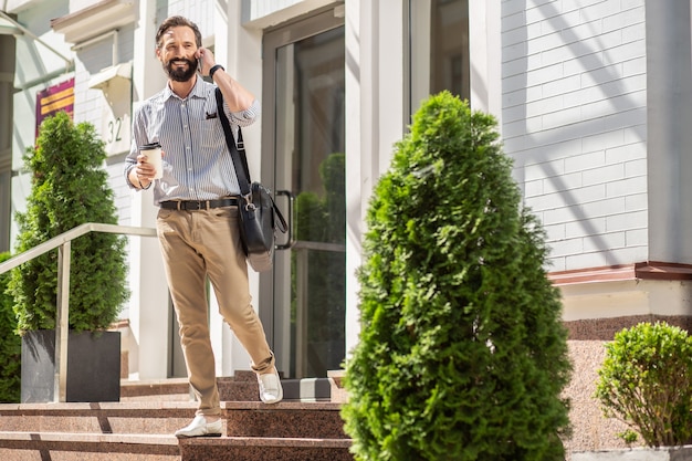 Keep me posted. Joyful bearded man talking on phone while going to work