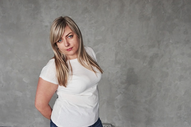 Keeping hands behind. Young white woman  standing against grey space