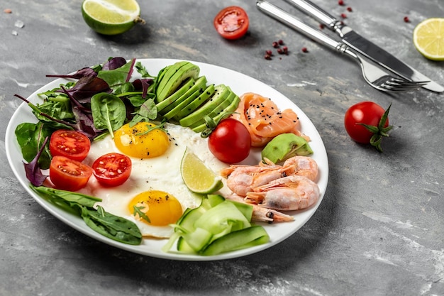 Ketogenic breakfast Keto low carb salmon boiled shrimps prawns fried eggs fresh salad tomatoes cucumbers and avocado top view Low carb diet concept high fat diet