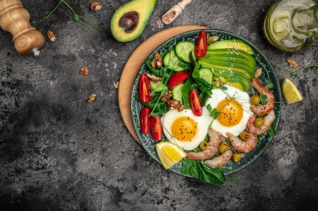 Photo ketogenic diet breakfast shrimps prawns soft fried egg fresh salad tomatoes cucumbers and avocado on a dark background keto paleo lunch top view