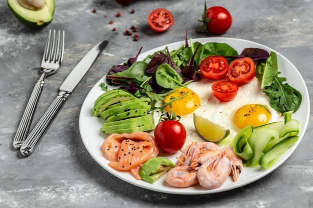 Ketogenic Low Carbohydrate Breakfast salmon, boiled shrimps, prawns, fried eggs, fresh salad, tomatoes, cucumbers and avocado. top view.