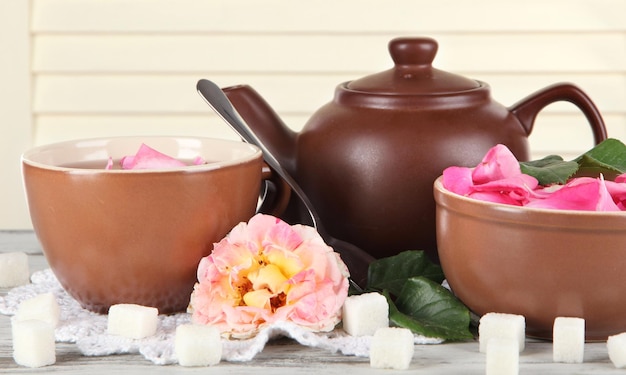 Kettle and cup of tea from tea rose on board on napkin on wooden background