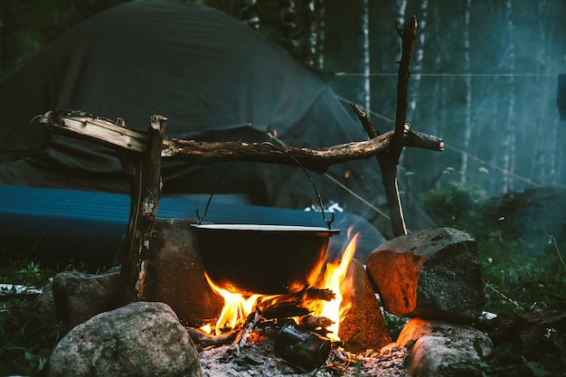 Kettle on fire near tent in forest at night