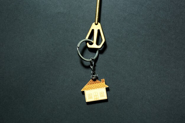 Key chain in the shape of house with key on a black background. Building, design, project, moving to new home, mortgage, deposit, rent and purchase real estate. Copy space