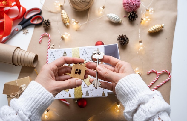 Key to house with keychain on cozy home in gift box with Christmas decor packaging Pack present for New Year Christmas Building project moving to new house mortgage rent purchase real estate