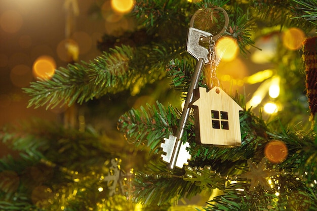 Key to the house with a keychain is hanging on the Christmas tree. A gift for New Year, Christmas. Building, design, project, moving to new house, mortgage, rent and purchase real estate. Copy space