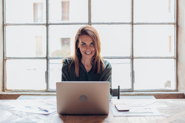 Key to success is your positive attitude at work portrait of a caucasian businesswoman smiling while sitting at her desk in front of laptop at office desk