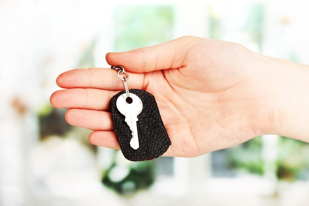 Key with leather trinket in hand on window background