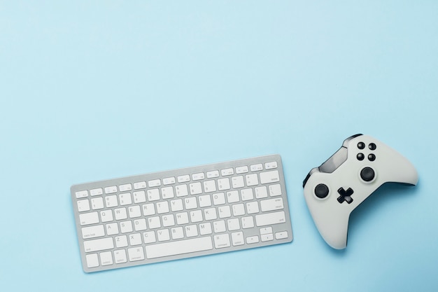 Keyboard and gamepad on a blue background. The concept of computer games, entertainment, gaming, leisure. Flat lay, top view