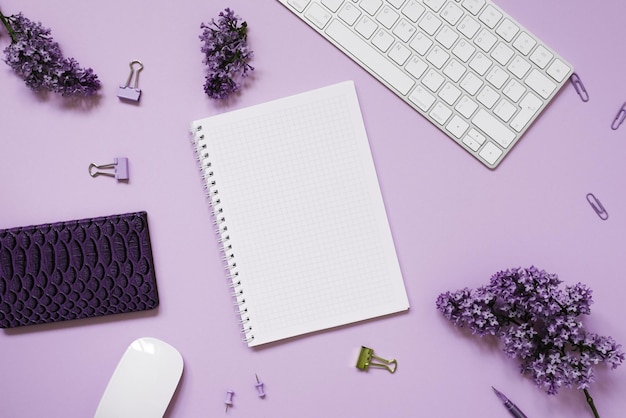 Keyboard and mouse notebooks pen a bouquet of lilacs on a purple background Purple spring flowers