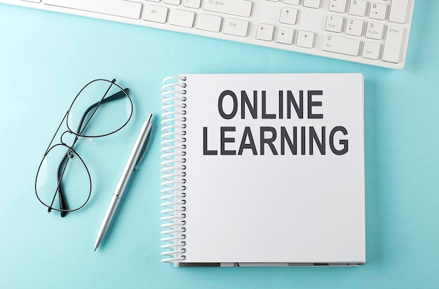 Keyboard, notebook,pen and glasses on the blue background with text ONLINE LEARNING