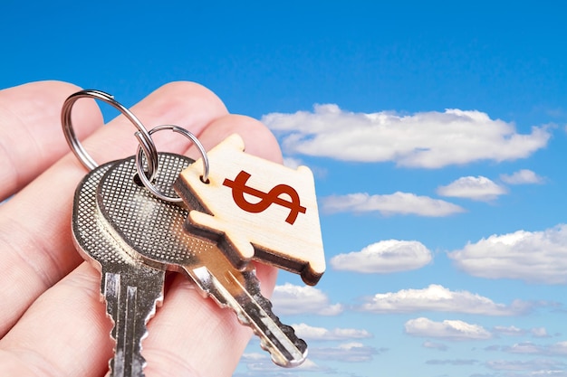 The keys to the new apartment in the hand of a man against the blue sky with clouds