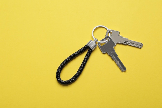 Keys with black leather keychain on yellow background top view Space for text