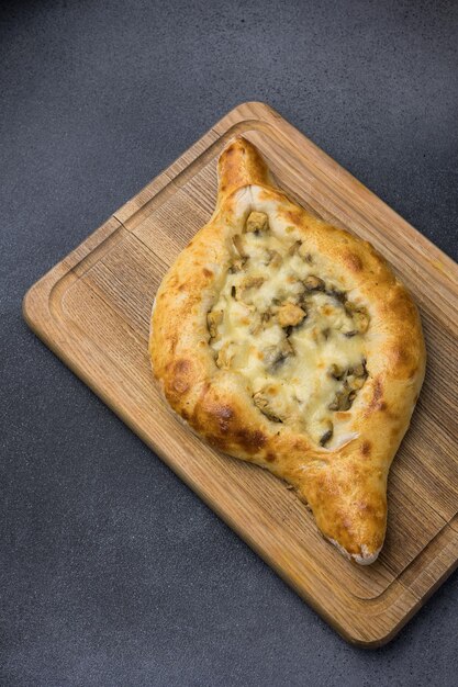 Photo khachapuri with cheese and mushrooms on a wooden cutting board