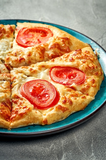 Khachapuri with salty melted cheese and tomato in a plate Concrete background