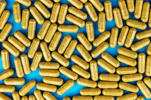 Khaki yellow pills capsules on blue paper Full frame background