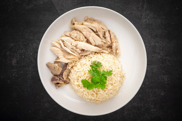 Khao Mun Gai, Thai food, rice steamed with chicken soup serve with chicken, soup and sauce on dark tone texture background, top view