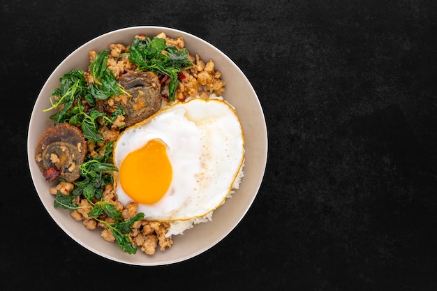 Khao Pad Ka Prao Kai Yeow Ma Kai Dao Thai food streamed rice with basil stir fried century egg mince pork and fried egg in ceramic plate on dark tone texture background top view