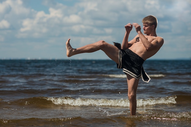 Kickboxer kicks in the open air in summer against the sea