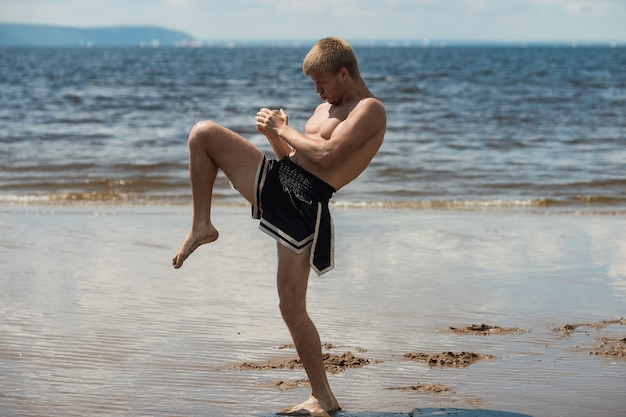 Kickboxer kicks in the open air in summer against the sea.