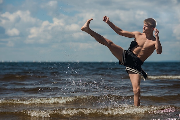 Kickboxer kicks in the open air in summer against the sea