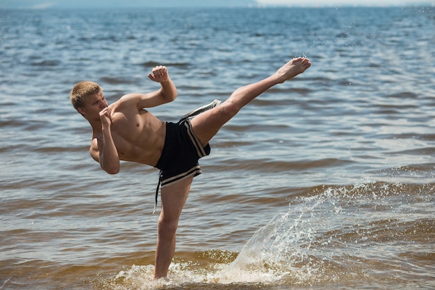 Kickboxer kicks in the open air in summer against the sea.