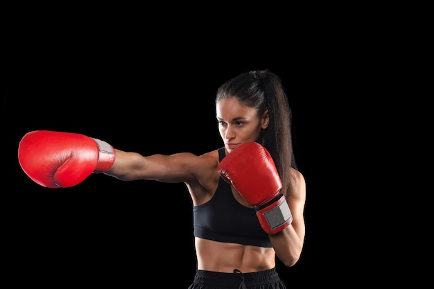 Kickboxing woman in activewear and red kickboxing gloves on black background performing a martial arts kick. Sport exercise, fitness workout.