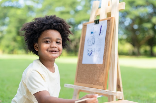 Kid artist African American little boy draw pictures and painting watercolor on white paper in park