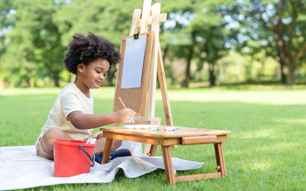 Kid artist African American little boy draw pictures and painting watercolor on white paper in park