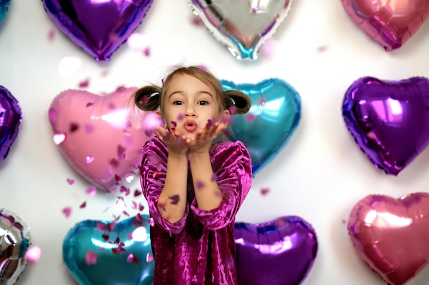 Kid blows confetti in the shape of hearts from palms while looking at the camera