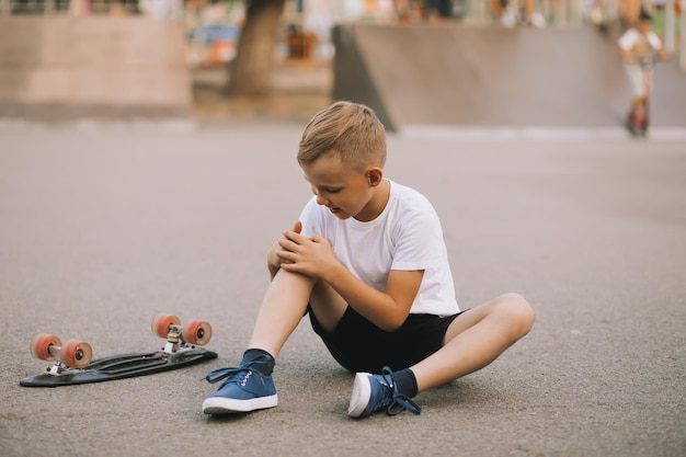 Kid boy teenager in a special area in skatepark fell and hurt his knee Child performs tricks Summer sport activity concept