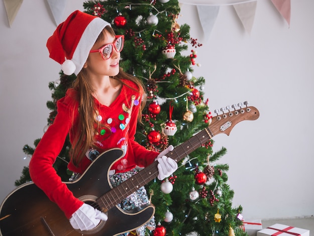 Kid celebrate Christmas by struming the guitar in house, A girl plays a song with a smile on Christmas Day