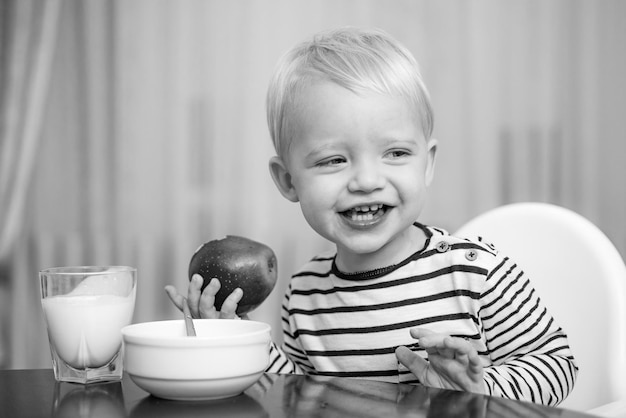 Kid cute boy sit at table with plate and food Healthy food Boy cute baby eating breakfast Baby nutrition Eat healthy Toddler having snack Healthy nutrition Vitamin concept Child eat apple