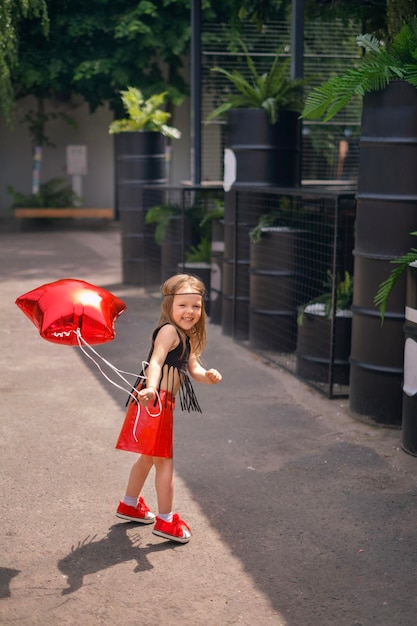 KId dressed in rock style in sneakers and skirt runs with balloon