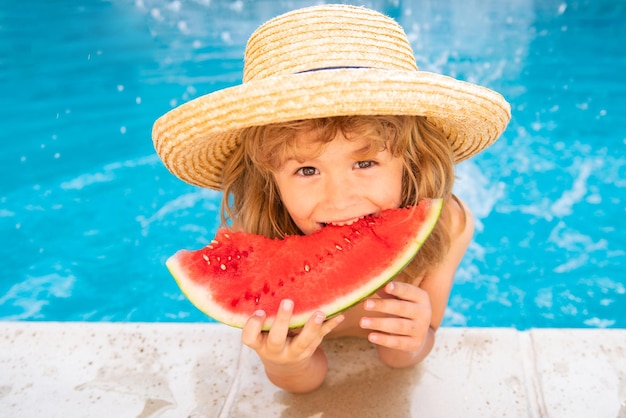 Kid eats watermelon in the pool cute boy eating slice of red watermelon on the beach happy caucasian...