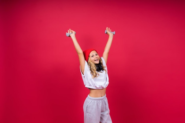 Kid girl doing fitness exercises with dumbbells on red background