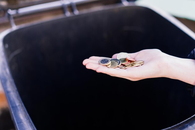 A kid girl hand throws a euro coins into a trash can dumpster street shot