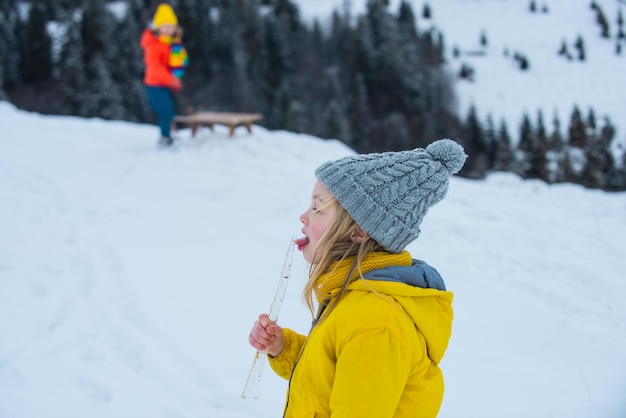 Kid girl lick icicle and eating snow in winter. Winter kids fun.