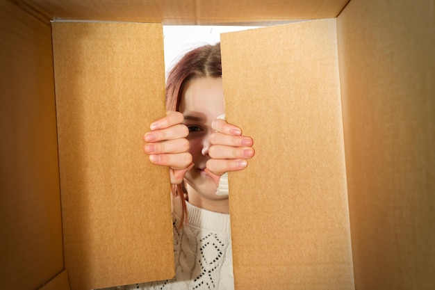 Kid girl teenager unpacking and opening carton box and looking inside with surprise