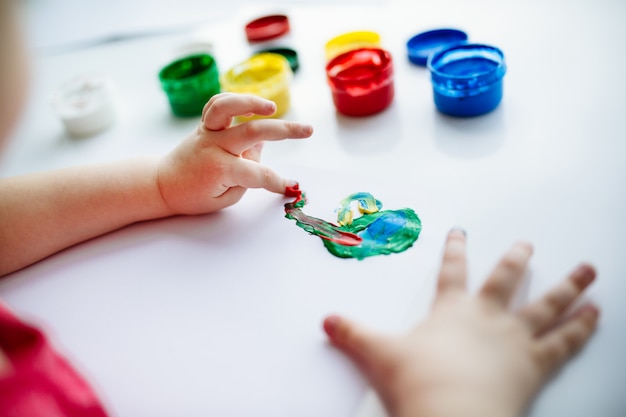 Kid hands start painting at the table with art supplies